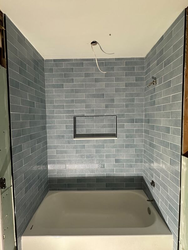 Bathtub surround in blue subway tile running to the ceiling, with fluted accent tiles, a darker blue band above the tub and a recessed niche with dark trim