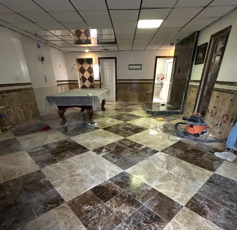 Finished basement with a polished dark and light Emperador marble floor laid in a diagonal checkerboard pattern and a pool table