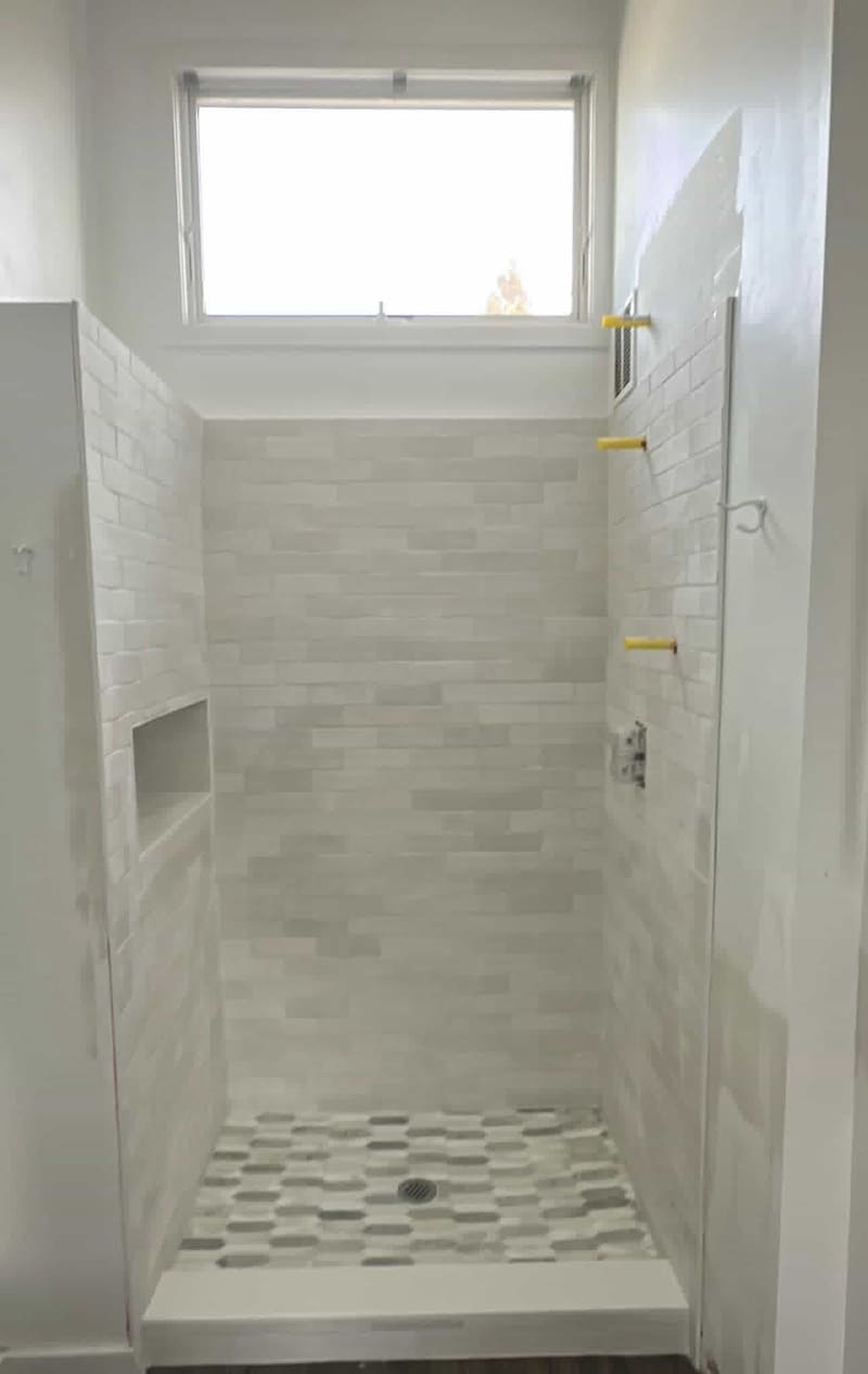 Walk-in shower with soft white subway tile walls, a recessed niche and a grey and white elongated hexagon marble mosaic floor
