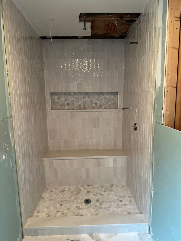 Walk-in shower with vertical glossy beige tile, a full-width built-in bench, a long recessed niche with hex marble mosaic and a hex marble mosaic floor
